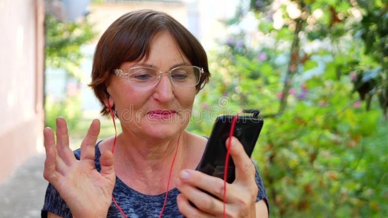 La mujer mayor escucha música por los auriculares rojos