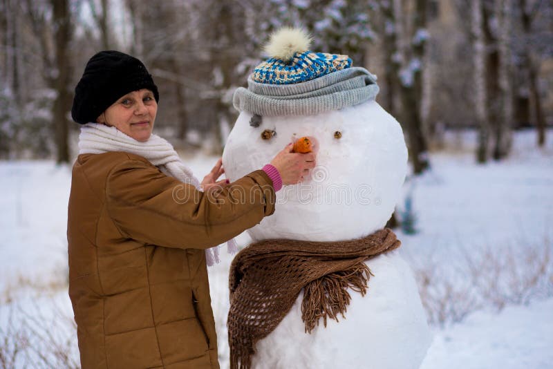 La mujer mayor feliz esculpe y abraza un muñeco de nieve real grande en invierno imagen de archivo La mujer mayor feliz esculpe y abraza un muñeco de nieve real grande en invierno imagen de archivo
