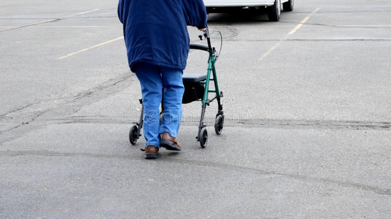 La mujer mayor utiliza a un caminante mientras que camina afuera en un estacionamiento almacen de video