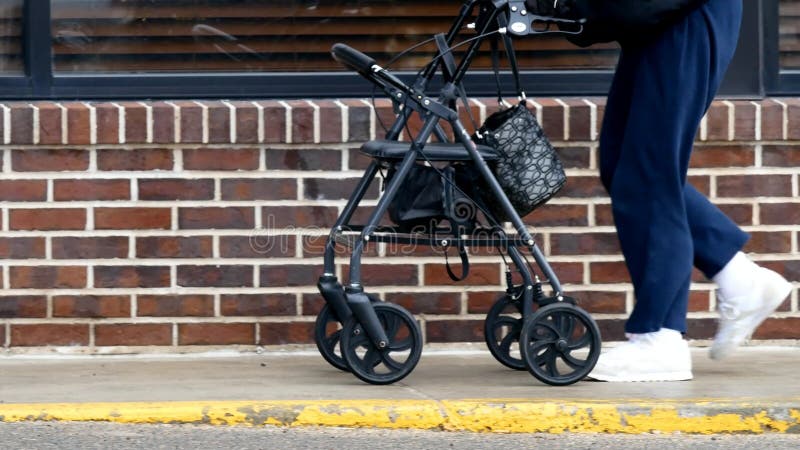 La mujer mayor utiliza a un caminante mientras que camina en una acera al lado de un edificio metrajes