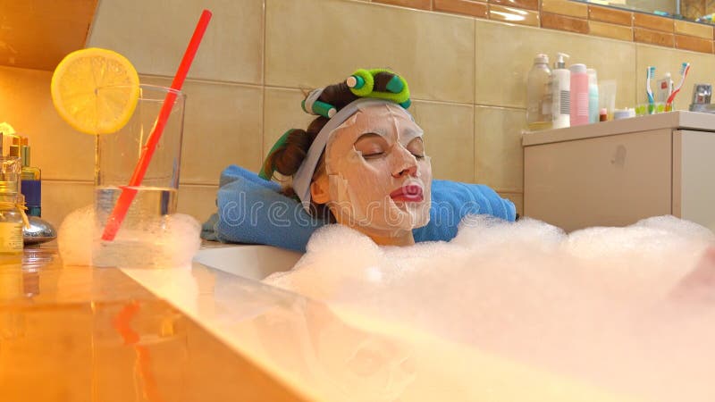 La mujer morena hermosa que lleva la mascarilla cosmética se relaja en baño espumoso Tratamiento de la belleza en casa foto de archivo libre de regalías La mujer morena hermosa que lleva la mascarilla cosmética se relaja en baño espumoso Tratamiento de la belleza en casa foto de archivo libre de regalías