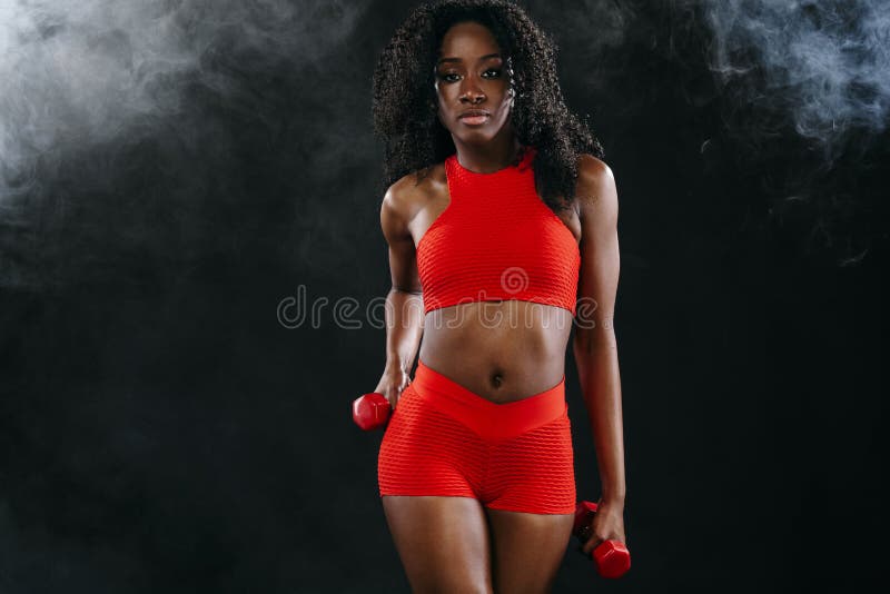 La mujer negra apta deportiva en ropa de deportes roja, atleta de la piel con pesas de gimnasia hace aptitud que ejercita en fond fotos de archivo La mujer negra apta deportiva en ropa de deportes roja, atleta de la piel con pesas de gimnasia hace aptitud que ejercita en fond fotos de archivo