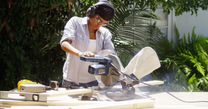 La mujer negra que hacía la madera del corte de las mejoras para el hogar con una tabla vio foto de archivo libre de regalías La mujer negra que hacía la madera del corte de las mejoras para el hogar con una tabla vio foto de archivo libre de regalías