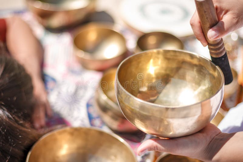 Woman playing a singing bowls also known as Tibetan Singing Bowls, Himalayan bowls. Making sound massage at beautiful sunny day. Woman playing a singing bowls also known as Tibetan Singing Bowls, Himalayan bowls. Making sound massage at beautiful sunny day.