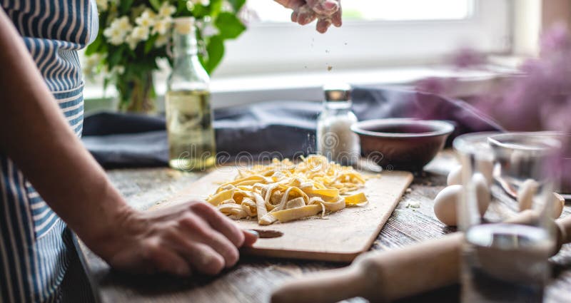 La mujer rocia cuidadosamente harina con fideos caseros frescos. el concepto de cocinar pasta hecha a mano en un ambiente acogedor imagen de archivo