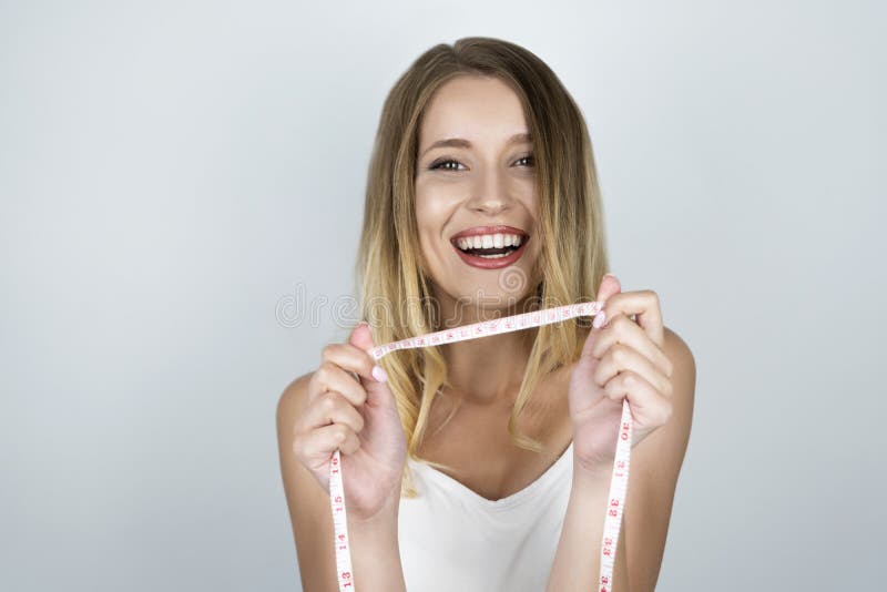 La mujer rubia atractiva joven parece feliz llevando a cabo centímetro en su fondo aislado blanco de las manos fotografía de archivo La mujer rubia atractiva joven parece feliz llevando a cabo centímetro en su fondo aislado blanco de las manos fotografía de archivo