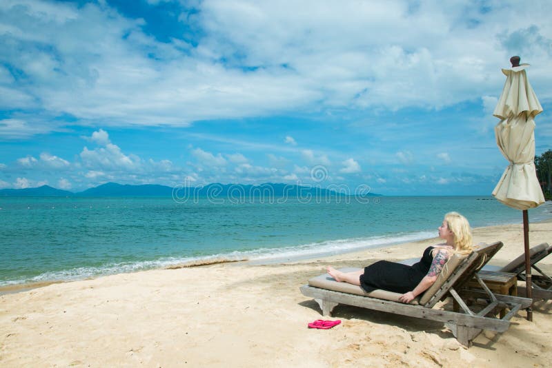 La mujer rubia está mintiendo en un deckchair en la playa imagen de archivo libre de regalías La mujer rubia está mintiendo en un deckchair en la playa imagen de archivo libre de regalías