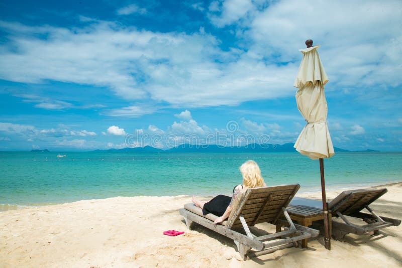 La mujer rubia está mintiendo en un deckchair en la playa imagen de archivo La mujer rubia está mintiendo en un deckchair en la playa imagen de archivo