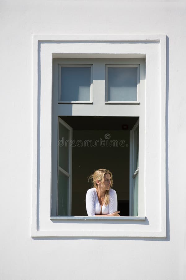 La mujer rubia hermosa mira hacia fuera de ventana abierta, de la pared blanca y del marco de ventana blanco fotos de archivo La mujer rubia hermosa mira hacia fuera de ventana abierta, de la pared blanca y del marco de ventana blanco fotos de archivo