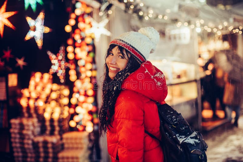 La mujer sonriente joven hermosa disfruta invierno de la nieve en feria de la Navidad en sombrero que lleva de la ciudad de la no fotografía de archivo libre de regalías La mujer sonriente joven hermosa disfruta invierno de la nieve en feria de la Navidad en sombrero que lleva de la ciudad de la no fotografía de archivo libre de regalías