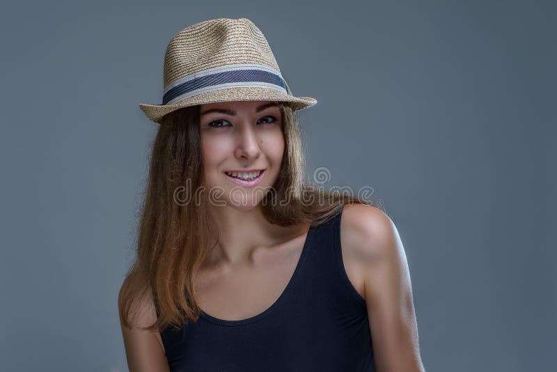La mujer sonriente joven hermosa en sombrero y camisa negra presentando está aislando elegante en fondo gris en un cierre del est imagenes de archivo La mujer sonriente joven hermosa en sombrero y camisa negra presentando está aislando elegante en fondo gris en un cierre del est imagenes de archivo