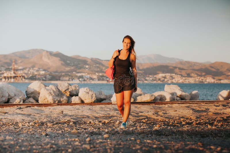 La mujer sonriente que camina en la orilla de mar con deportes viste fotografía de archivo La mujer sonriente que camina en la orilla de mar con deportes viste fotografía de archivo