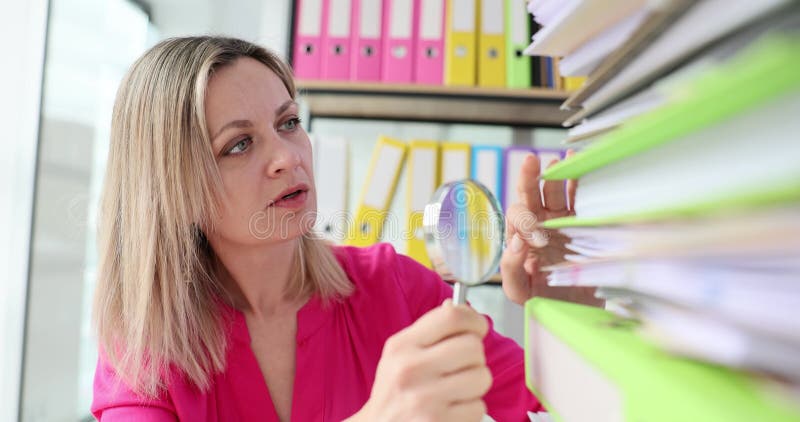 La mujer usa la lupa para buscar en los archivos de papel en la oficina almacen de metraje de vídeo