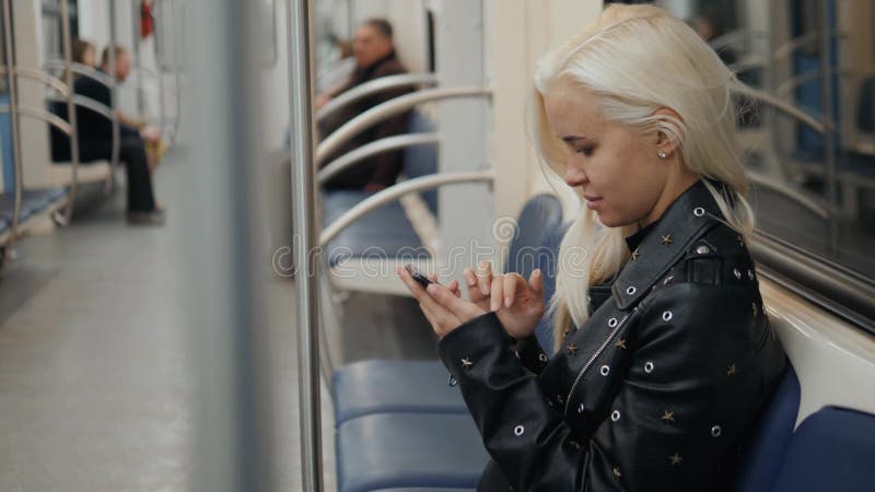 La mujer utiliza un smartphone en la chica joven del subterráneo en estudiante del transporte del tren almacen de video