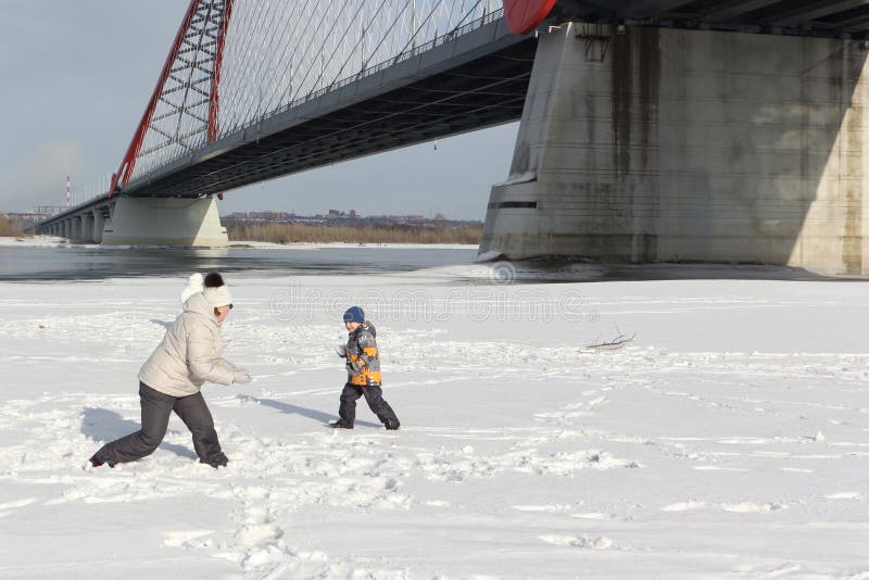 La mujer y el niño pequeño que juegan bolas de nieve en el riverbank imágenes de archivo libres de regalías La mujer y el niño pequeño que juegan bolas de nieve en el riverbank imágenes de archivo libres de regalías
