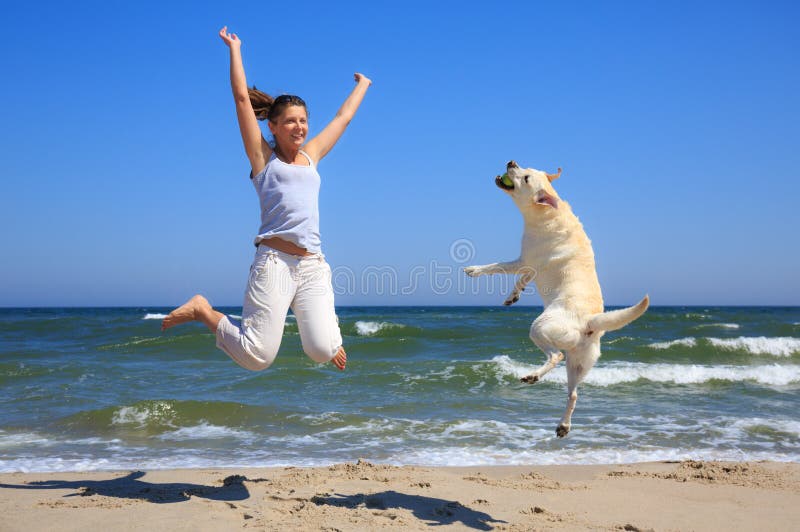 La mujer y el perro crían Labrador que salta en la playa