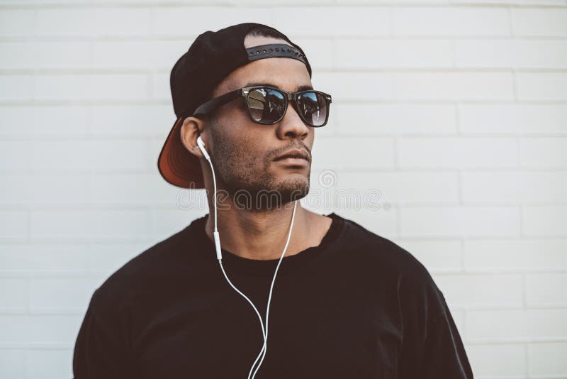 Handsome young African man in headphones looking away and looking serious while standing in front of the stoned wall outdoors. Handsome young African man in headphones looking away and looking serious while standing in front of the stoned wall outdoors