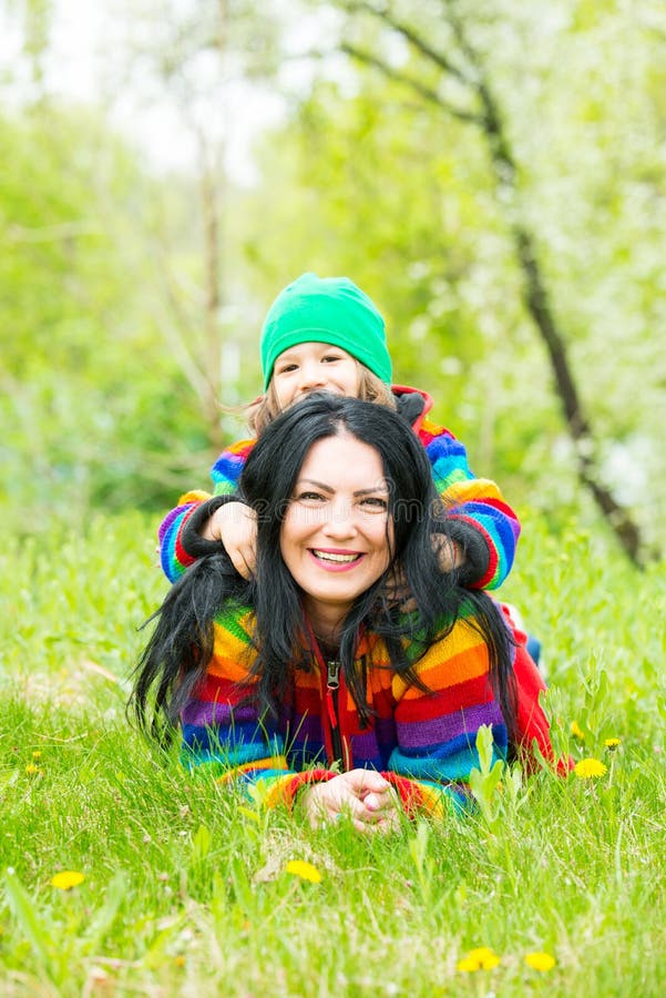 Mother giving piggyback to her son and laying on grass in park. Mother giving piggyback to her son and laying on grass in park