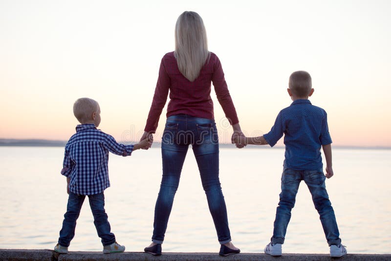 La mère et deux fils marchent sur la promenade et observent le coucher du soleil photo libre de droits La mère et deux fils marchent sur la promenade et observent le coucher du soleil photo libre de droits