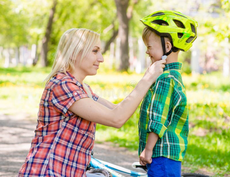 La mère heureuse habille son casque de bicyclette de fils images libres de droits La mère heureuse habille son casque de bicyclette de fils images libres de droits