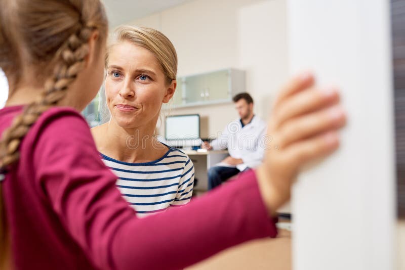 La mère parlant a effrayé la petite fille dans médecins Office image stock La mère parlant a effrayé la petite fille dans médecins Office image stock