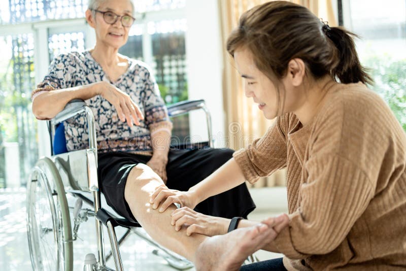 Asian senior mother in wheelchair,receiving a leg massage from her daughter,old women enjoy,pain relief,elderly people suffer from sore muscles,female caregiver use a gentle massage hand to relaxation. Asian senior mother in wheelchair,receiving a leg massage from her daughter,old women enjoy,pain relief,elderly people suffer from sore muscles,female caregiver use a gentle massage hand to relaxation