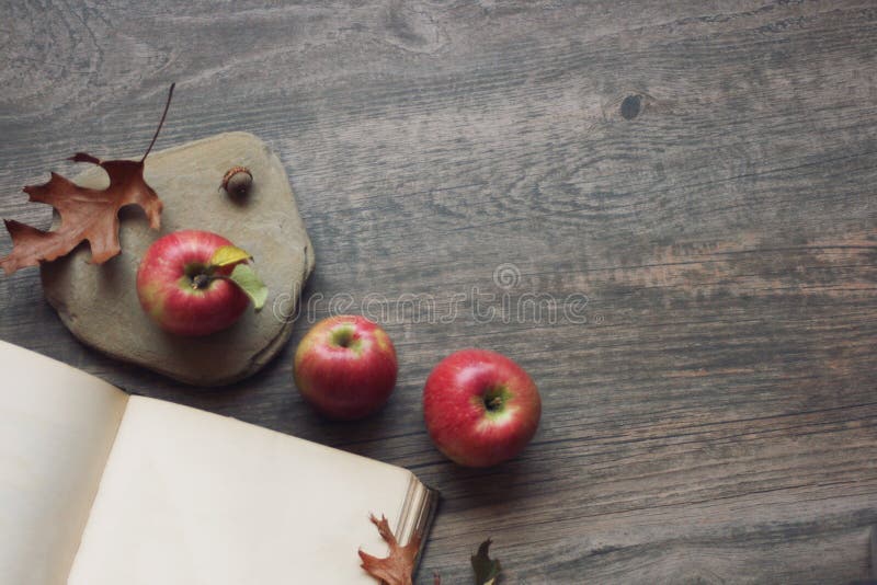 La natura morta di autunno con tre mele, libro aperto e rimane il fondo di legno rustico
