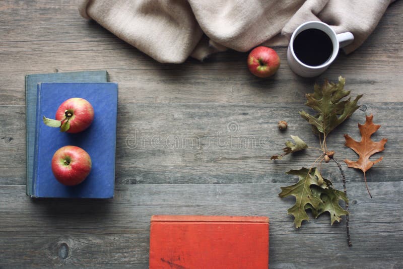 La natura morta di stagione di autunno con le mele, i libri, la coperta, la tazza di caffè nero e la caduta rossi rimane il fondo