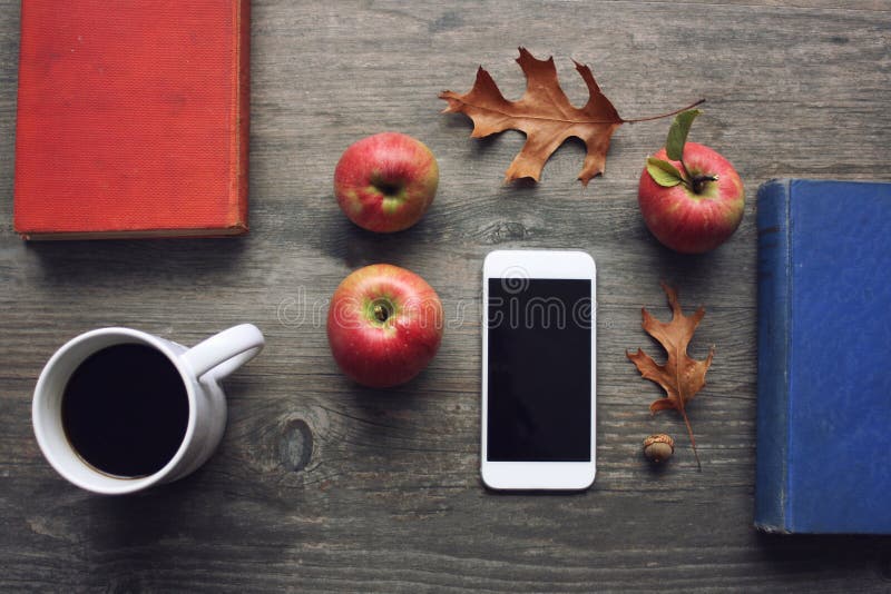 La natura morta di stagione di autunno con le mele, i libri, il dispositivo mobile, la tazza di caffè nero e la caduta rossi rima