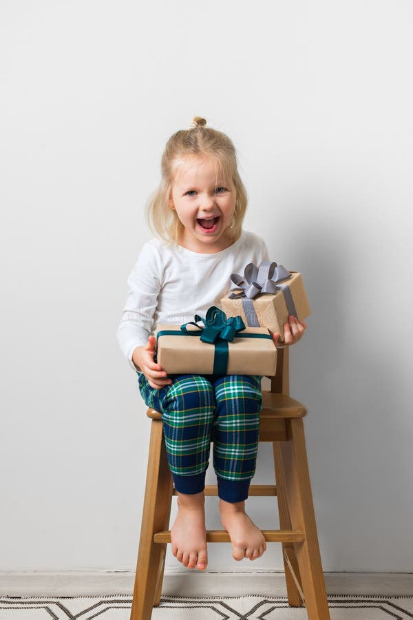 La Navidad escandinava del minimalismo y concepto del A?o Nuevo con el ni?o - ni?a con la pila de caja de regalo en una silla en fotografía de archivo La Navidad escandinava del minimalismo y concepto del A?o Nuevo con el ni?o - ni?a con la pila de caja de regalo en una silla en fotografía de archivo