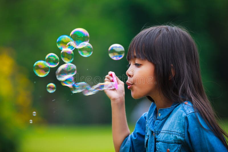 La niña asiática está soplando burbujas de un jabón imagen de archivo