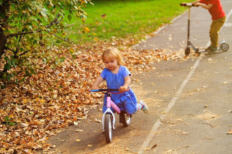 La niña en runbike y el muchacho en la vespa en otoño, niños se divierten fotografía de archivo La niña en runbike y el muchacho en la vespa en otoño, niños se divierten fotografía de archivo