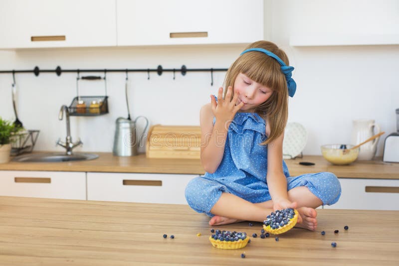 La niña linda en vestido azul come una torta y se lame los fingeres en una tabla fotografía de archivo libre de regalías La niña linda en vestido azul come una torta y se lame los fingeres en una tabla fotografía de archivo libre de regalías