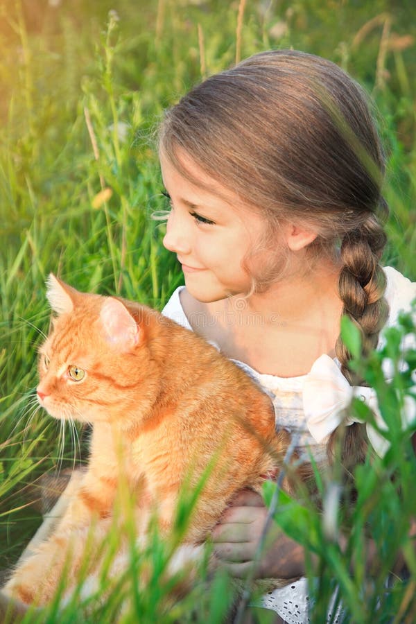 La niña linda está sosteniendo un gato rojo que se sienta en la hierba fotos de archivo La niña linda está sosteniendo un gato rojo que se sienta en la hierba fotos de archivo