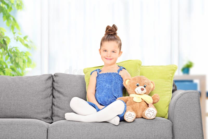 La niña linda que se sienta con el peluche refiere un sofá fotografía de archivo libre de regalías La niña linda que se sienta con el peluche refiere un sofá fotografía de archivo libre de regalías