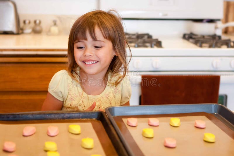 La niña orgullosa acabó de colocar la pasta de la galleta en la bandeja del horno foto de archivo