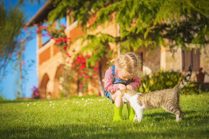 Little Girl and cat play on a green meadow in spring beautiful day on a farm. Little Girl and cat play on a green meadow in spring beautiful day on a farm