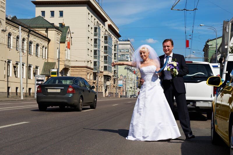La novia y el novio divertidos cogen el taxi en la calle