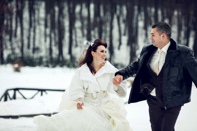 La novia y el novio se divierten que corre a través de un parque en el weath de la nieve fotos de archivo libres de regalías La novia y el novio se divierten que corre a través de un parque en el weath de la nieve fotos de archivo libres de regalías