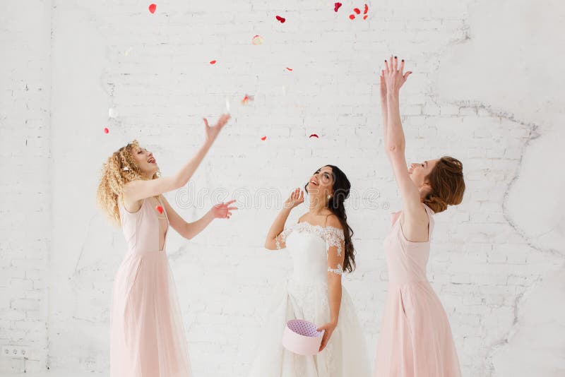 La novia y las damas de honor lanzan para arriba los pétalos en el estudio blanco del desván Retrato lleno-lenght fotografía de archivo libre de regalías La novia y las damas de honor lanzan para arriba los pétalos en el estudio blanco del desván Retrato lleno-lenght fotografía de archivo libre de regalías