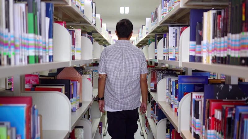 La opinión trasera el estudiante universitario camina en biblioteca almacen de metraje de vídeo