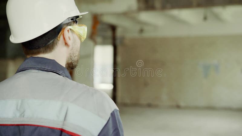 La opinión trasera el inspector se vistió en uniforme, el casco de protección protector y lentes caminando en el solar y la compr