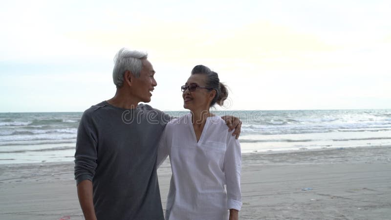 La pareja asiática de ancianos jubilados descansan tranquilamente caminando en la luna de miel de la playa al atardecer