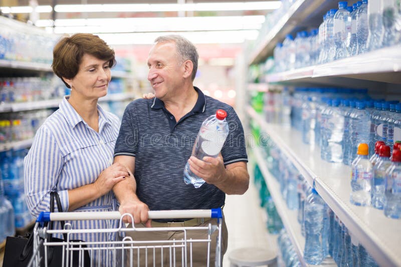 La pareja de ancianos compra una botella de agua potable en el departamento de supermercados imagen de archivo libre de regalías
