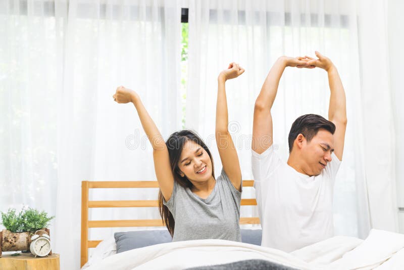 La pareja de matrimonios preciosa asiática joven despierta estirar junta en cama en dormitorio Subida y brillo, día perezoso de l fotos de archivo