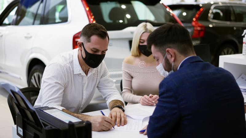 La pareja de máscaras compra de un auto nuevo firmando el contrato en la sala de espectáculos almacen de video