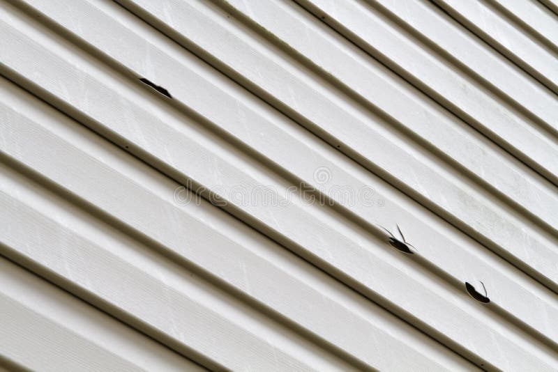 Angled shot of a vinyl siding panel on a house damaged by a summer hail storm. The hail that did this damage was golf ball size hail stones. Angled shot of a vinyl siding panel on a house damaged by a summer hail storm. The hail that did this damage was golf ball size hail stones.