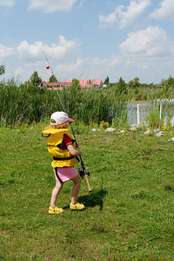 La pequeña muchacha caucásica rubia adorable sostiene la caña de pescar y va al lago Ella lleva en chaleco salvavidas gafas de so fotografía de archivo La pequeña muchacha caucásica rubia adorable sostiene la caña de pescar y va al lago Ella lleva en chaleco salvavidas gafas de so fotografía de archivo