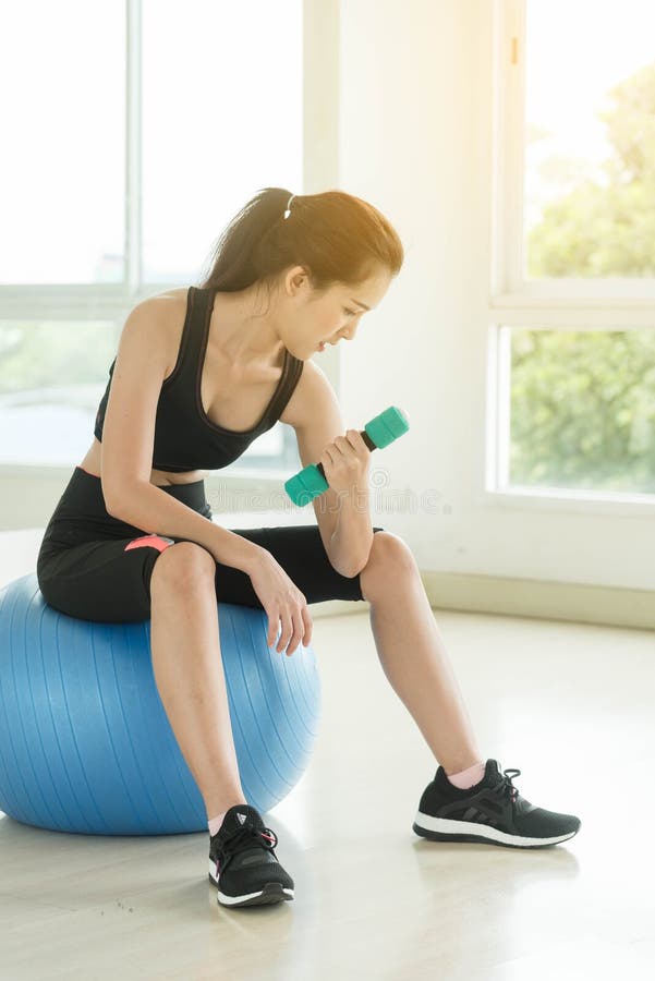 La pesa de gimnasia hermosa joven de la elevación de la mujer se sienta en bola imagenes de archivo