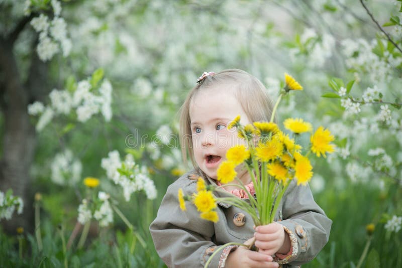 La petite fille avec la trisomie 21 tient un bouquet des pissenlits